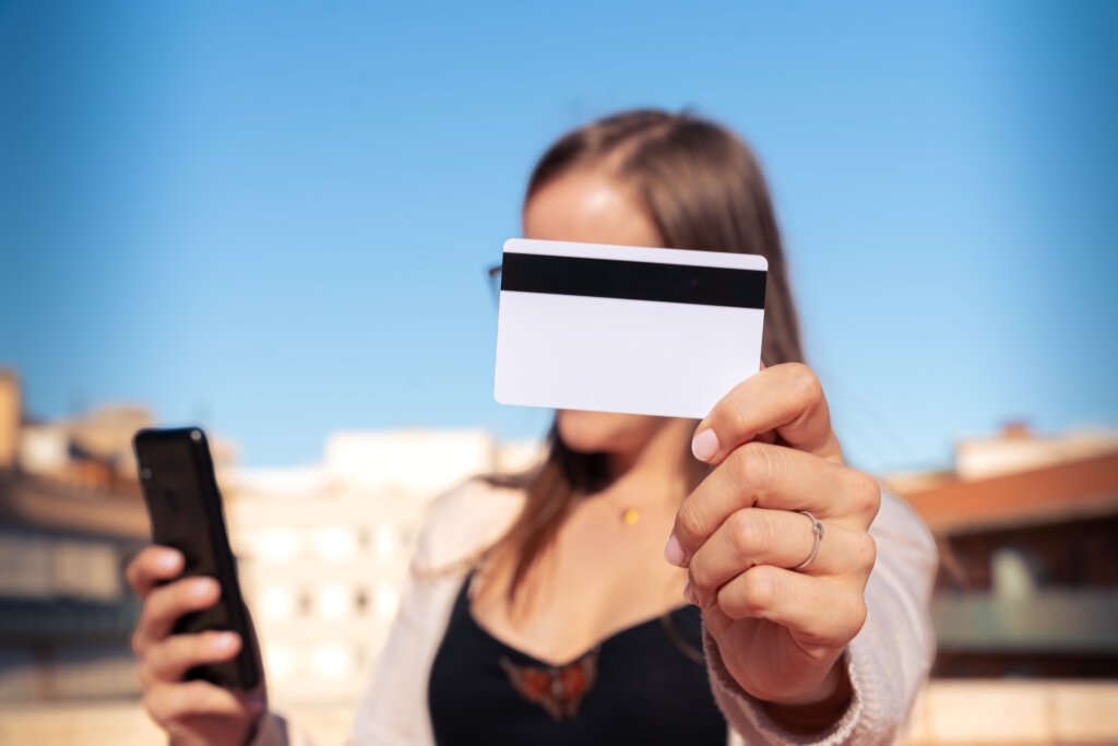 young smiling woman paying by credit card smartphone outdoors